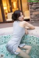 A woman in a gray dress sitting in a bathtub.