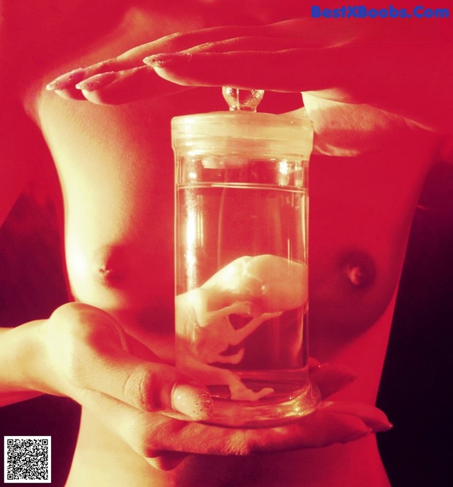 A woman holding a glass jar with a baby inside of it.