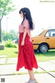 A woman in a pink shirt and red skirt standing on a sidewalk.