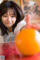 A young woman sitting at a table with an orange.