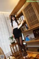 A woman in a white shirt and black skirt standing in front of a book shelf.