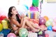 A woman sitting on the floor surrounded by balloons and presents.