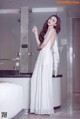 A woman in a white dress standing in a bathroom.