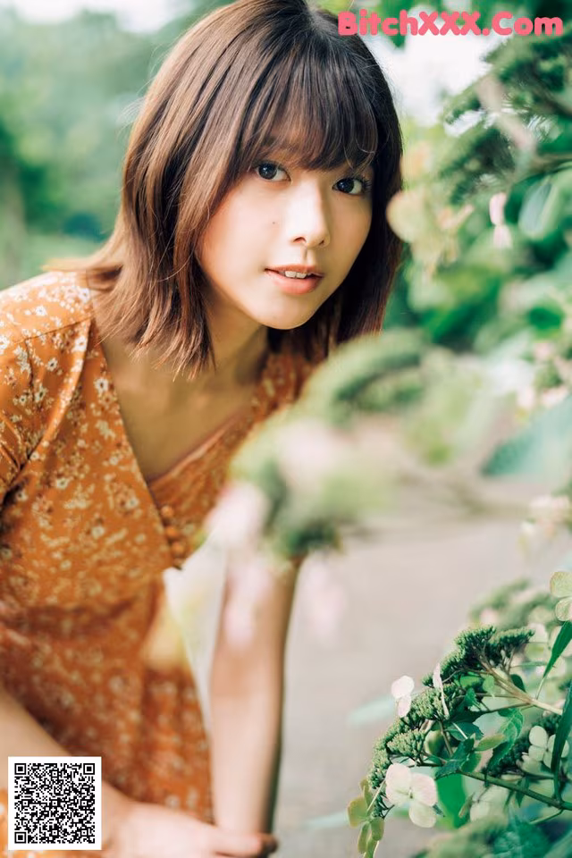 A woman in an orange dress leaning against a tree.