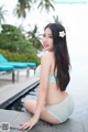 A woman in a blue bikini sitting by a pool.