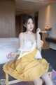 A woman in a yellow dress sitting on a bed.