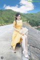 A woman in a yellow dress sitting on a concrete wall.