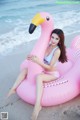 A woman sitting on an inflatable flamingo on the beach.