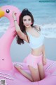 A woman in a blue top and pink shorts posing on an inflatable flamingo.